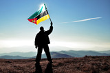 Fototapeta  - Successful silhouette man winner waving Mozambique flag on top of the mountain peak