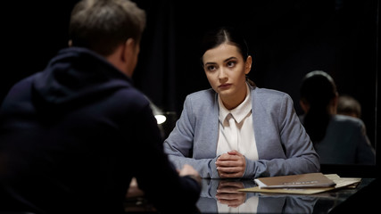 Woman police officer interrogating male suspect in dark room, mistrust, equality