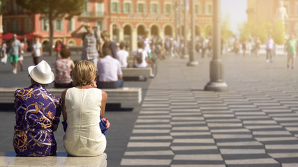 Two women having rest on bench, active life in city center, sunny summer day