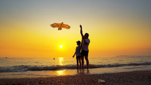 Father And Son Flying Kite On Sea Coast With Nice Orange Sky Sunset. Steadicam Shot
