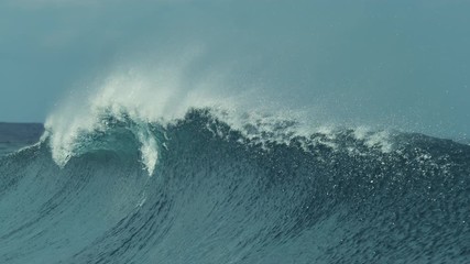 Wall Mural - SLOW MOTION, CLOSE UP: Glassy water sparkles in the sun as tiny droplets fly away from large barrel wave coming from the vast Pacific Ocean. Beautiful deep blue ocean wave splashing near exotic island