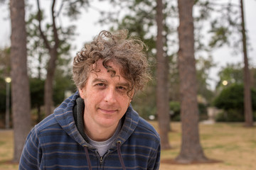 An attractive forty something man with long curly hair poses for a photo while out for a walk in the woods in winter.