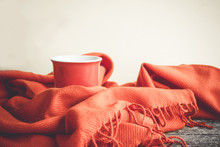 Cup Of Coffee Wrapped In An Orange Scarf On A Wooden Table And A Gray Background. Autumn Or Winter Concept. Copy Space