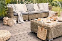 Wicker Patio Set With Beige Cushions Standing On A Wooden Board Deck. Breakfast On A Table On A Backyard Porch.