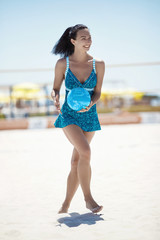 A girl in a blue sports dress with a volleyball ball, running on the sand on the volleyball court