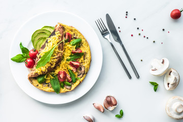 Wall Mural - flat lay with homemade omelette with cherry tomatoes, avocado pieces, spinach and cutlery on white marble surface