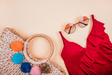 Wall Mural - Summer fashion flatlay with gradient round sunglasses, trendy straw bag with pompoms and red swimsuit with frills on the beige background. Perfect beach set for holidays on the sea. Marina style.