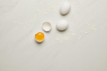 Wall Mural - top view of raw chicken eggs and flour on white marble tabletop