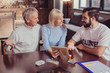 © Viacheslav Yakobchuk - Tell me about it. Attentive cute senior woman sitting with her husband by the table holding a photo and looking at a volunteer.