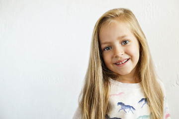 Portrait of happy little girl with long blonde hair smilng and showing positive emotions. Funny child with joyful facial expression. White isolated background, close up, copy space.