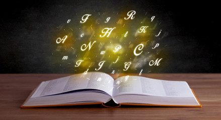 Wall Mural - Glowing yellow alphabet letters coming out of an open book 