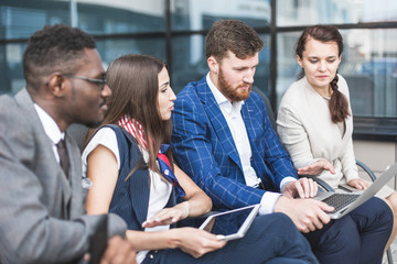 Wall Mural - Group of happy diverse male and female business people team in formal gathered around laptop computer in bright office against the background of a glass building