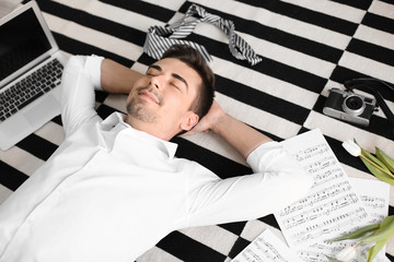 Wall Mural - Young man with laptop and music sheets lying on carpet