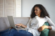 © Anatoliy Karlyuk - Sideways shot of attractive young African American woman watching movie online on her generic laptop while relaxing on couch at home alone after work. People, modern technology and leisure