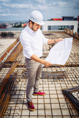 Wall Mural - young architect looking at paper plans on construction site. Details of construction building and workers