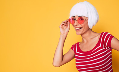 Sticker - Beautiful young woman in blonde wig and pink sunglasses having fun on orange background, fashion blonde posing