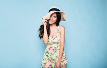 Portrait Of Cute Summer Brunette Woman In Hat And Colorful Dress, Stylish Girl Have A Fun And Posing On Blue Background