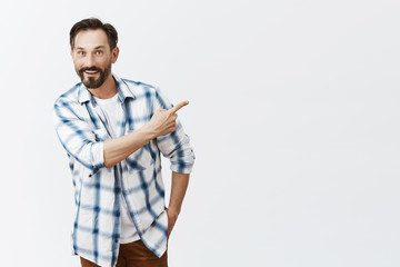 Wall Mural - Man showing friends his new tv, being proud he can afford it. Portrait of carefree relaxed and friendly handsome mature husband in checked shirt, pointing right and bending towards camera