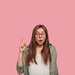 Poster - Disturbed youngster feels surprised, points with index finger upwards cant believe such sales exist, wears transparent glasses with red rim, isolated over pink studio wall. Omg, look above please!