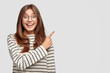 © wayhome.studio - Horizontal shot of joyful pleased good looking youngster points at upper right corner with index finger, invites you go there, dressed in casual clothes, poses against white background, blank space