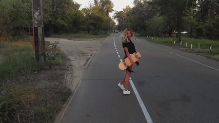 Wall Mural - A young girl in white shorts and a black T-shirt is riding on a skateboard at sunset in the evening. Sunset. Sports and fitness. Slow motion. Aerial Filming