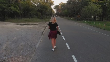 Wall Mural - A young girl in white shorts and a black T-shirt is riding on a skateboard at sunset in the evening. Sunset. Sports and fitness. Slow motion. Aerial Filming