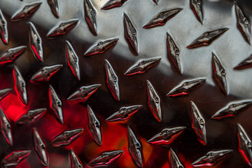 Close up of stainless steel sheet with diamond plate pattern and reflecting red lights / Metallic background