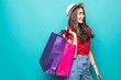 Portrait of an excited beautiful girl wearing dress and sunglasses holding shopping bags over blue background