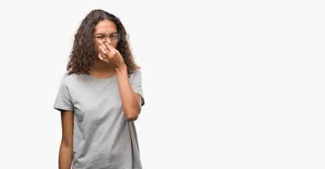 Canvas Print - Beautiful young hispanic woman wearing glasses smelling something stinky and disgusting, intolerable smell, holding breath with fingers on nose. Bad smells concept.