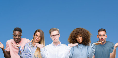 Canvas Print - Composition of group of friends over blue blackground clueless and confused expression with arms and hands raised. Doubt concept.