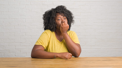 Wall Mural - Young african american woman sitting on the table at home looking stressed and nervous with hands on mouth biting nails. Anxiety problem.