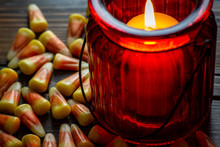 Candy Corn A Halloween Treat On A Wooden Table With A Red Glass Candle Holder Making Them Glow On Halloween Night