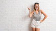 © Krakenimages.com - Young beautiful blonde woman over white brick wall smiling with happy face winking at the camera doing victory sign. Number two.