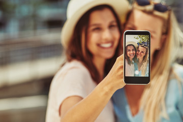 Wall Mural - Two young female friends taking selfies together outside in summ