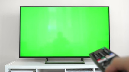 Watching tv with green screen at home interior. Push buttons on remote. Changing channels on television