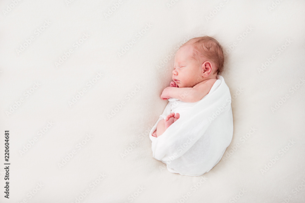 Cute newborn baby lies swaddled in a white blanket. Copy space and top view - obrazy, fototapety, plakaty 