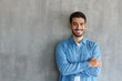 © Damir Khabirov - Portrait of smiling handsome man in blue shirt standing with crossed arms against gray textured wall with copy space