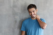 © Damir Khabirov - Close up beauty shot of young smiling man in casual blue t-shirt standing against gray textured wall