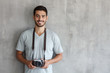 © Damir Khabirov - Portrait of smiling handsome male photographer in gray t shirt, holding his camera, standing against gray textured wall with copy space for your ads