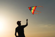 © ruslanshug - silhouette of healthy male in cap playing flying kite in autumn sunset