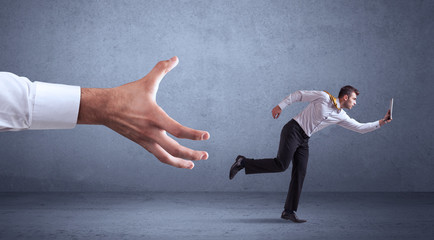 Wall Mural - Young miniature businessman running from a big hand with blueish grey background