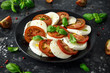 © grinchh - Caprese salad with tomatoes, mozzarella cheese and fresh basil leaves in a black plate. Italian food.