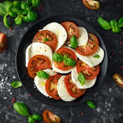 Wall Mural - Caprese salad with tomatoes, mozzarella cheese and fresh basil leaves in a black plate. Italian food.