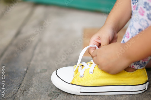 Photographie hand of children or kid girl learning and try tie shoelace on yellow shoe or sne
