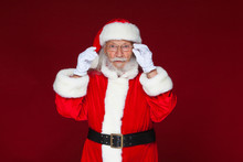 Christmas. Serious Santa Claus In White Gloves Adjusts Her Glasses And Stares Into The Camera. Isolated On Red Background.