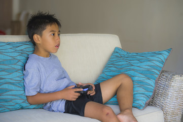 Canvas Print -  Latin young kid 8 years old excited and happy playing video game online holding remote controller enjoying having fun on couch in child gaming addiction