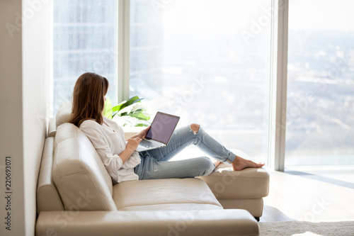Relaxed woman using laptop in luxury home living room with big window, enjoying Poster Mural XXL