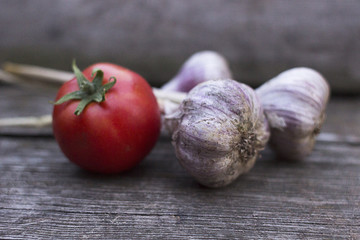 Ripe red tomato and garlic on an old wooden background. New crop