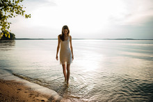 Woman In Summer Dress Standing On Seashore And Looking At Horizon. Young Beautiful Girl Standing In Water