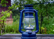 Old Blue Kerosene Lantern, With A Burning Wick On An Old Worn Wooden Table